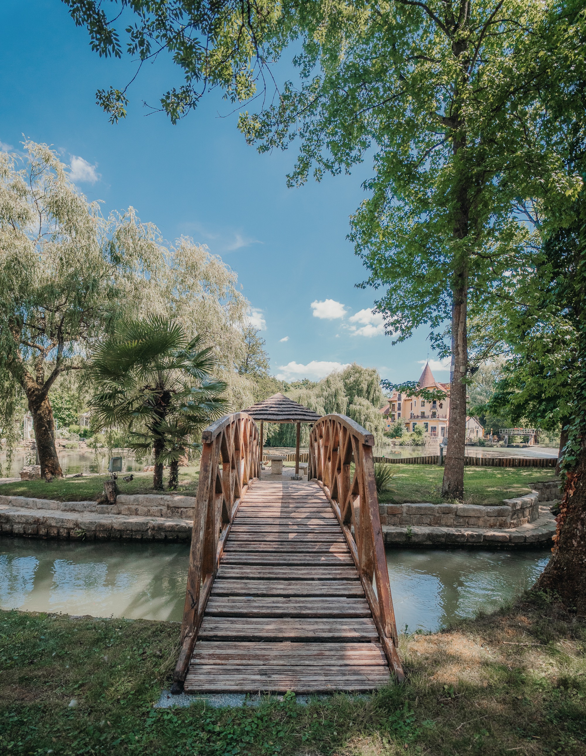 Le bâtiment principal d'Ora le Domaine reflété dans l'étang, entouré de saules pleureurs